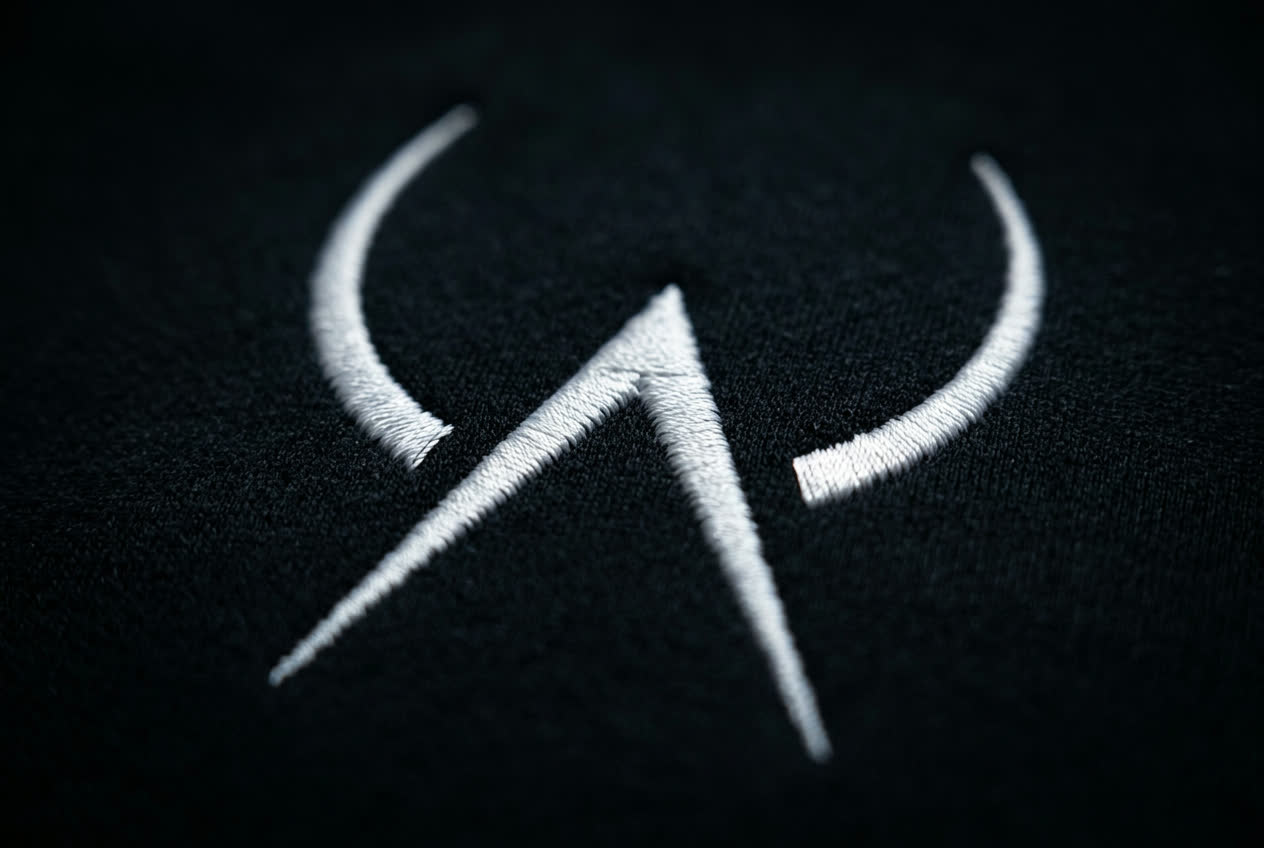 Close-up detail of the Huntress inverse-circle badge embroidered on black performance fabric